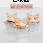 Three cute butterfly cakes dusted with icing sugar, and served on a white cake stand.