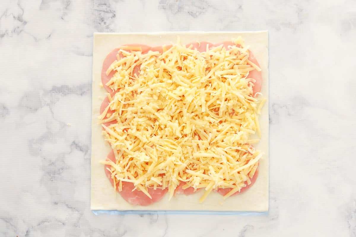 Grated cheese and ham slices on a sheet of puff pastry.