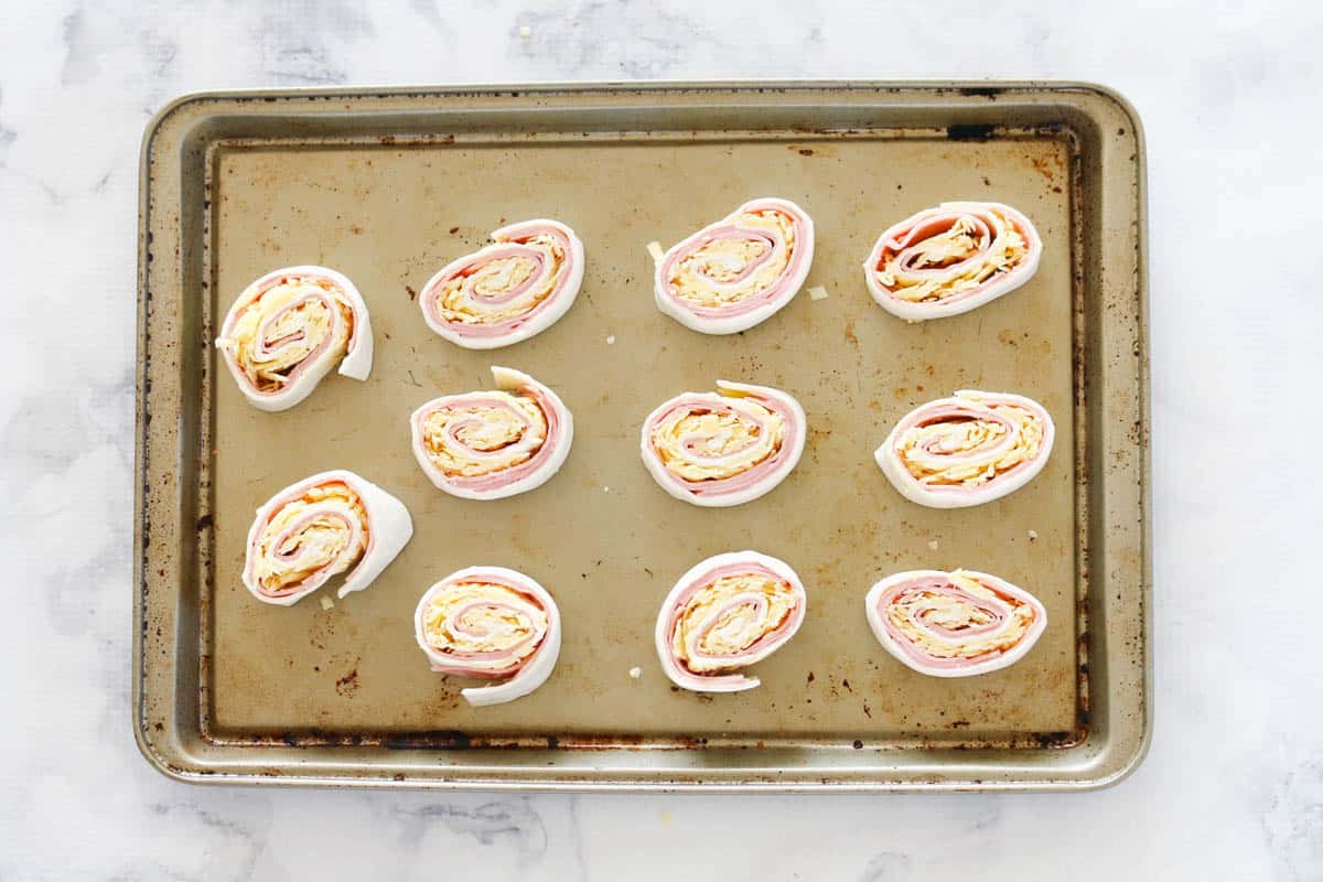 Sliced pinwheels with ham and cheese on a baking tray.