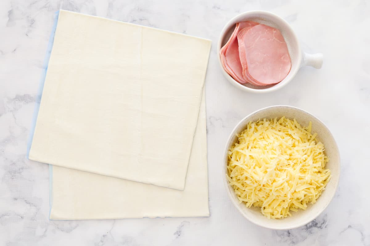Puff pastry, grated cheese and ham on a marble board.