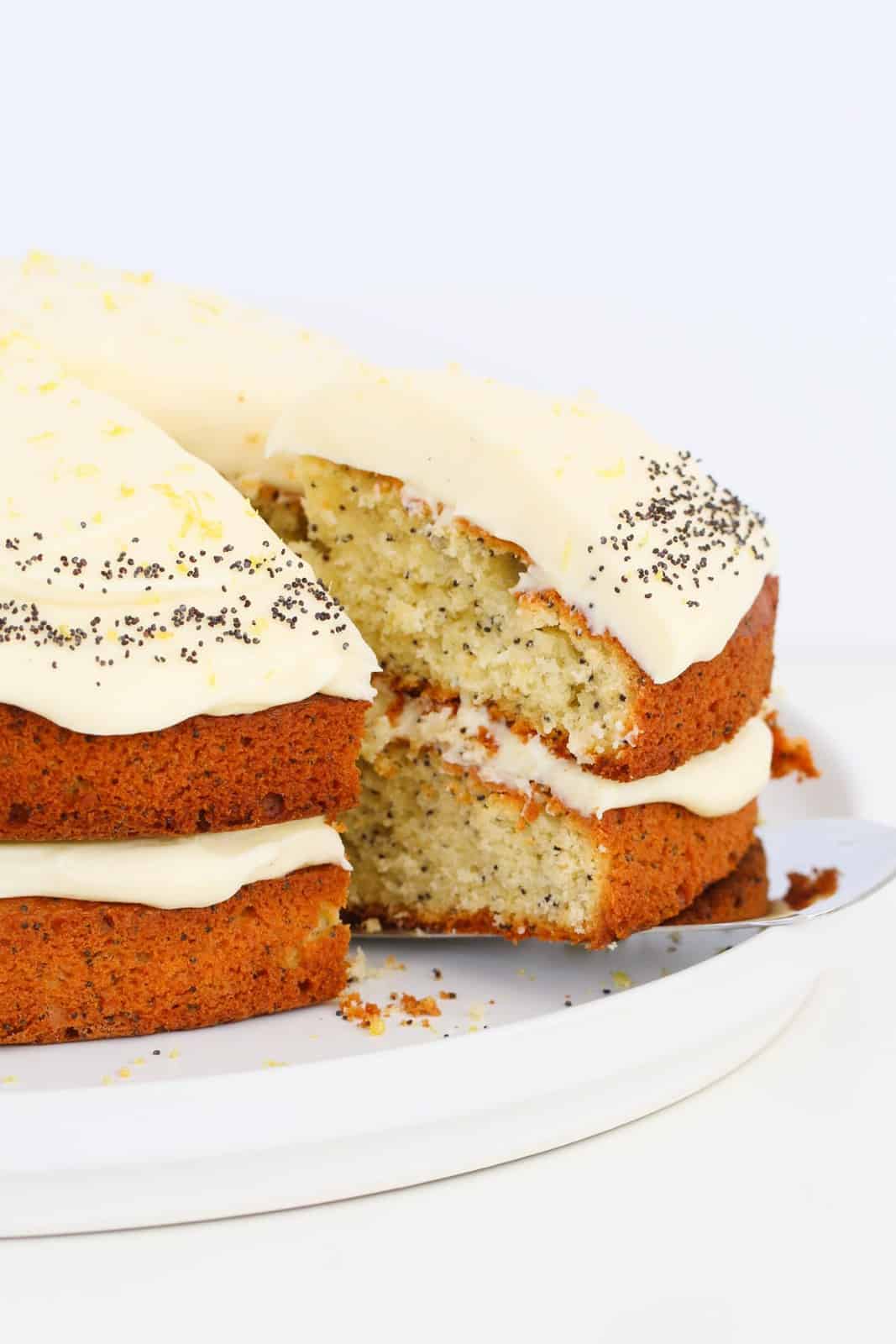 A slice of poppy seed cake with cream cheese frosting being removed from the rest of the cake.