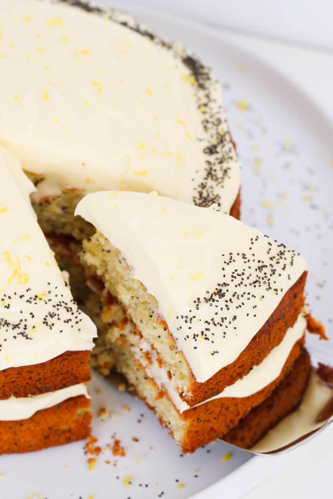 A slice of cream cheese frosted lemon and poppy seed cake being removed with a cake slice.