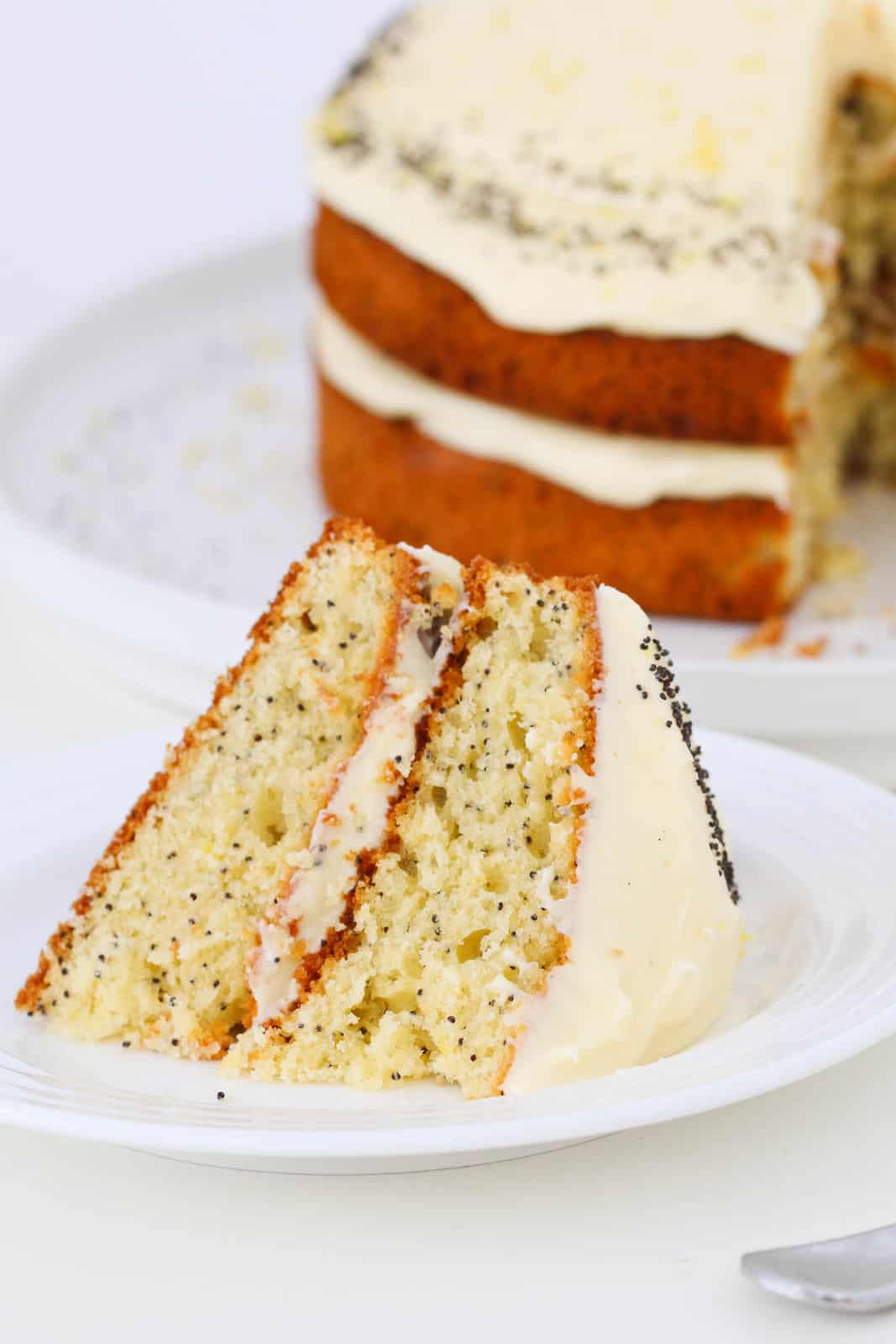 A slice of double layered lemon cake with poppy seeds and cream cheese frosting.
