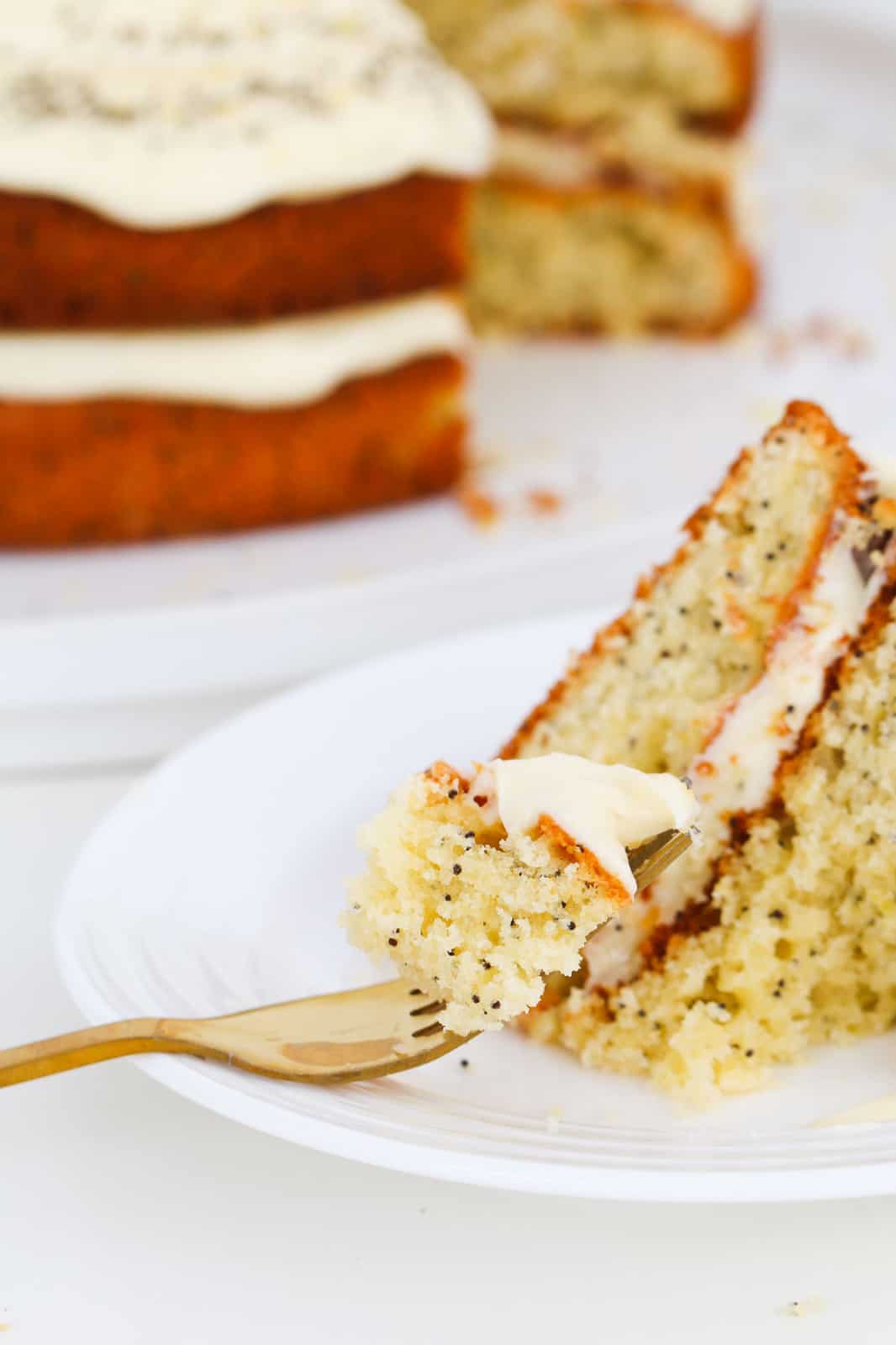 A fork with lemon and poppy seed cake with cream cheese frosting on a plate.