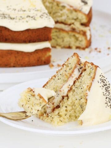 A fork with poppy seed cake with cream cheese frosting on a plate.