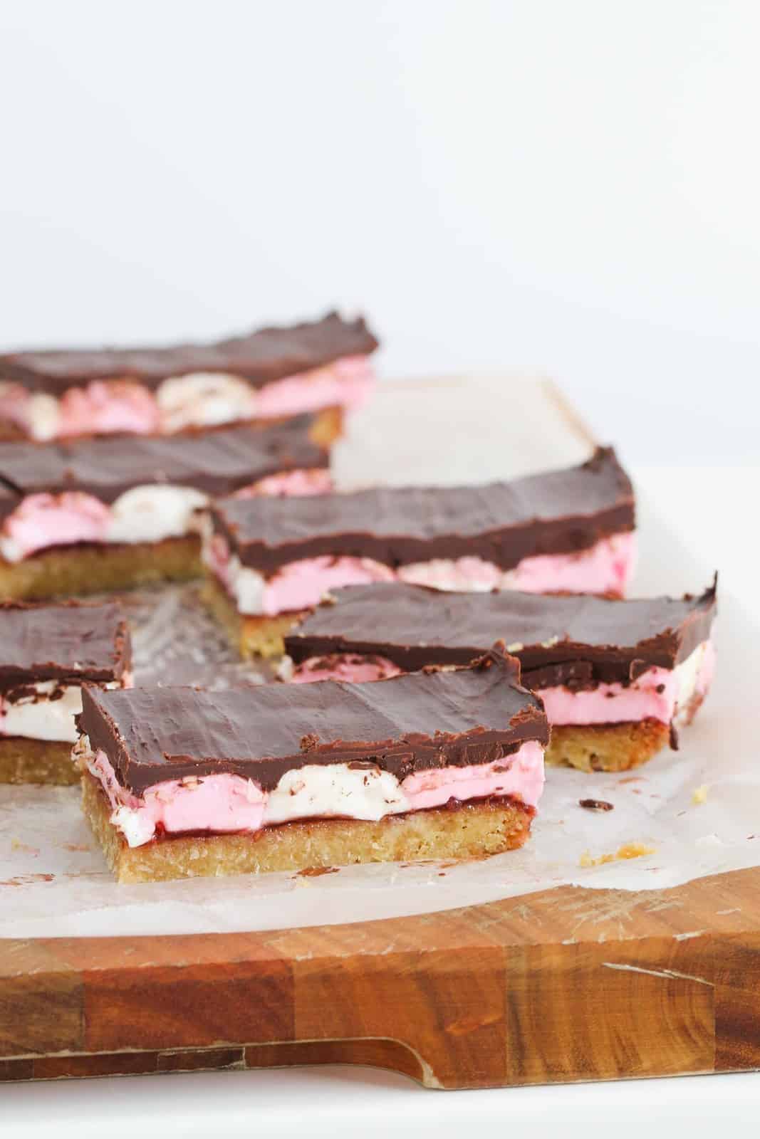 Pieces of wagon wheel slice on a chopping board with a layer of pink and white marshmallows in between.