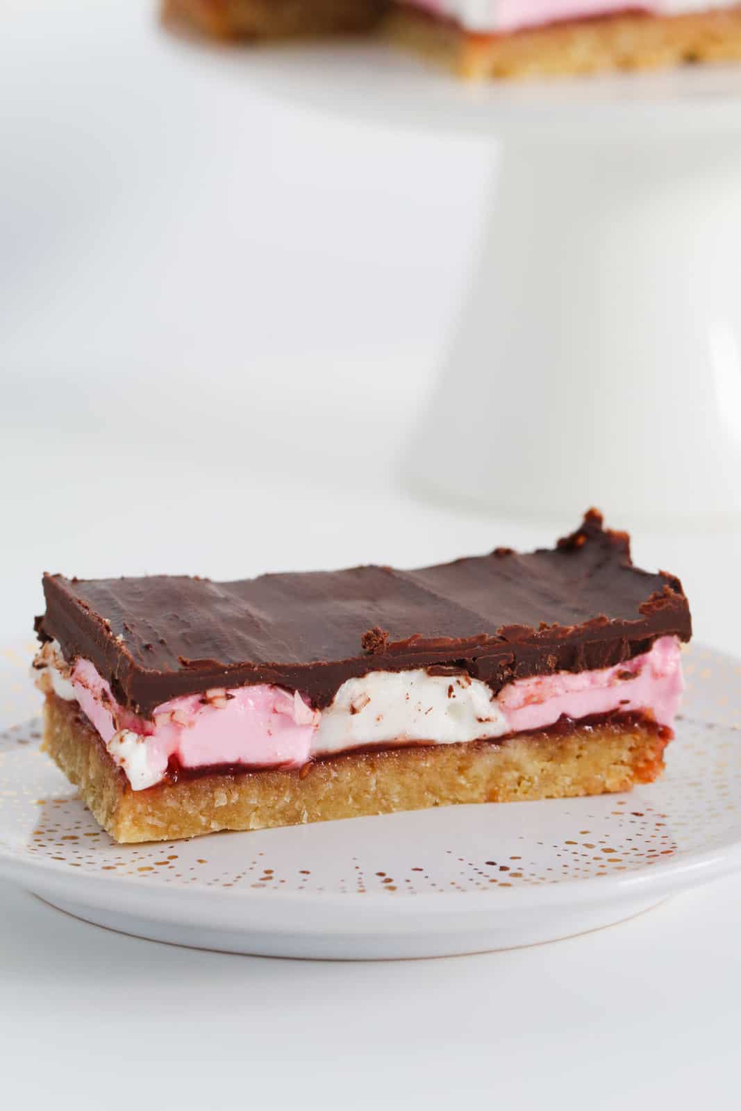 A piece of marshmallow slice on a plate showing layers of base, jam, marshmallows and chocolate.