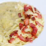 part of a white soup plate with a thick, chunky soup with a garnish of bacon and cheese