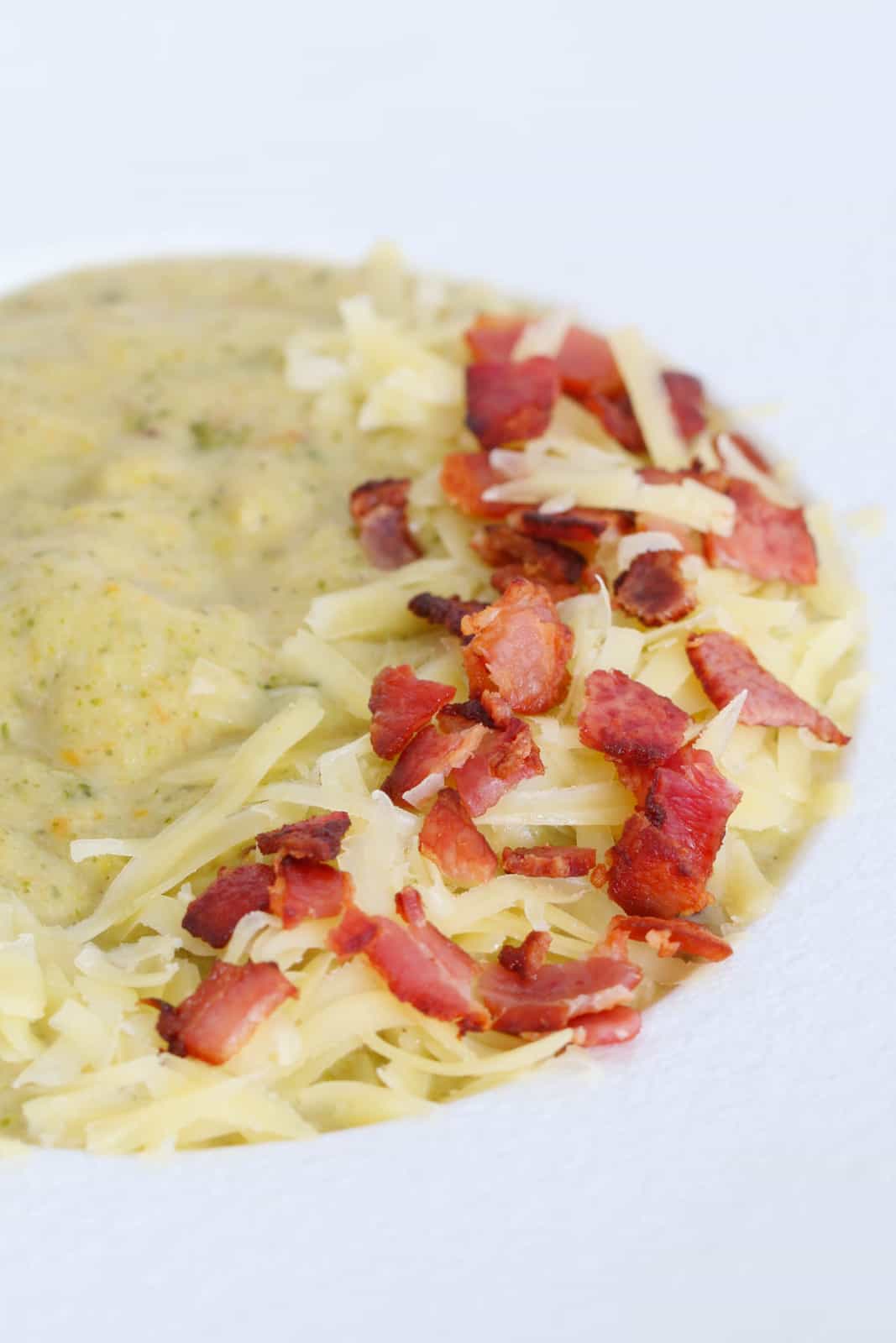 A white soup bowl filled with a thick, chunky soup with a garnish of bacon and cheese