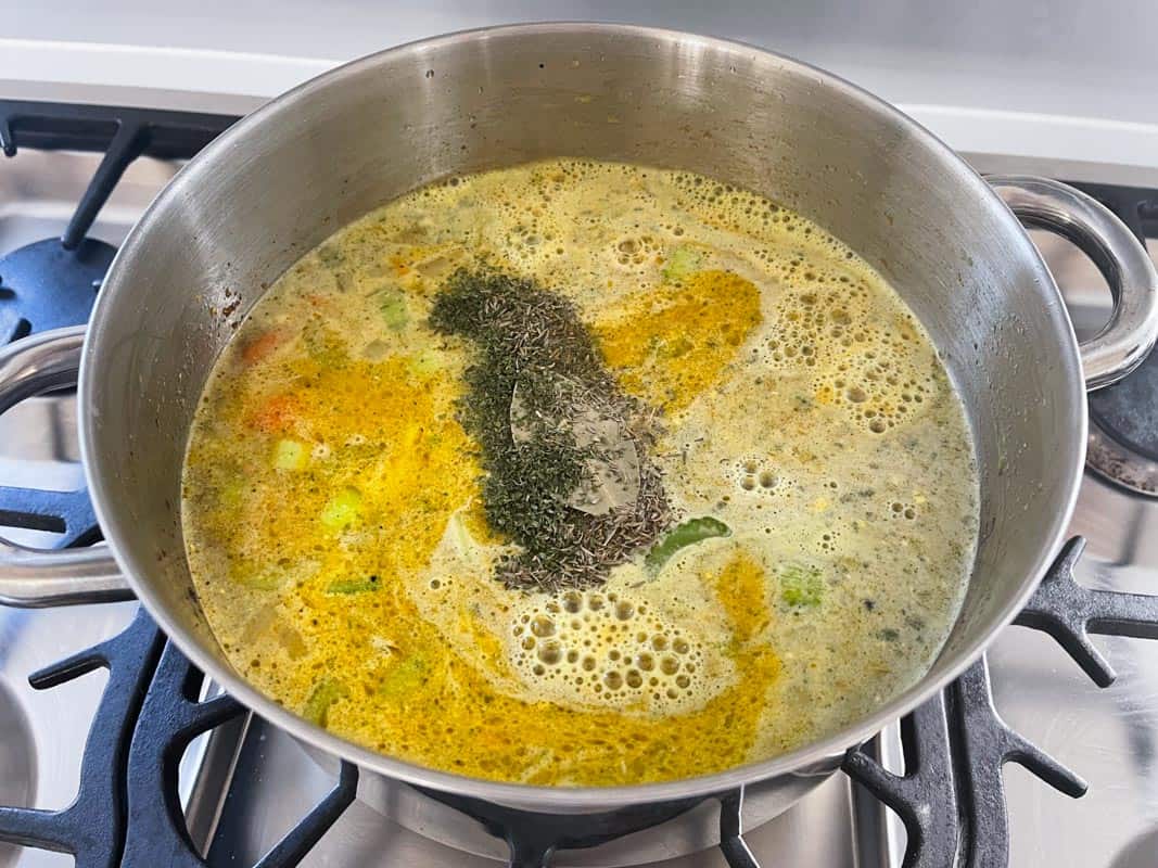 A stainless steel pot with stock and seasonings added to diced vegetables 