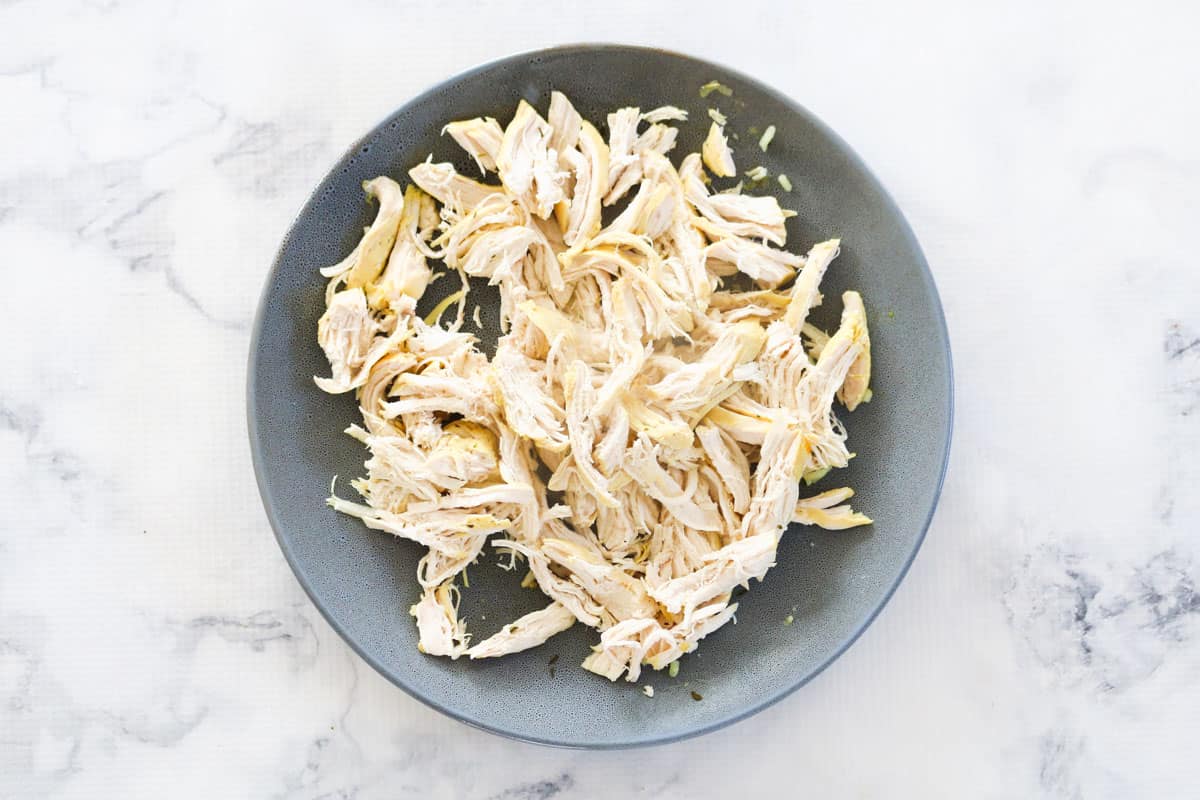 A grey bowl with coarsely shredded chicken breast meat on a marble bench top