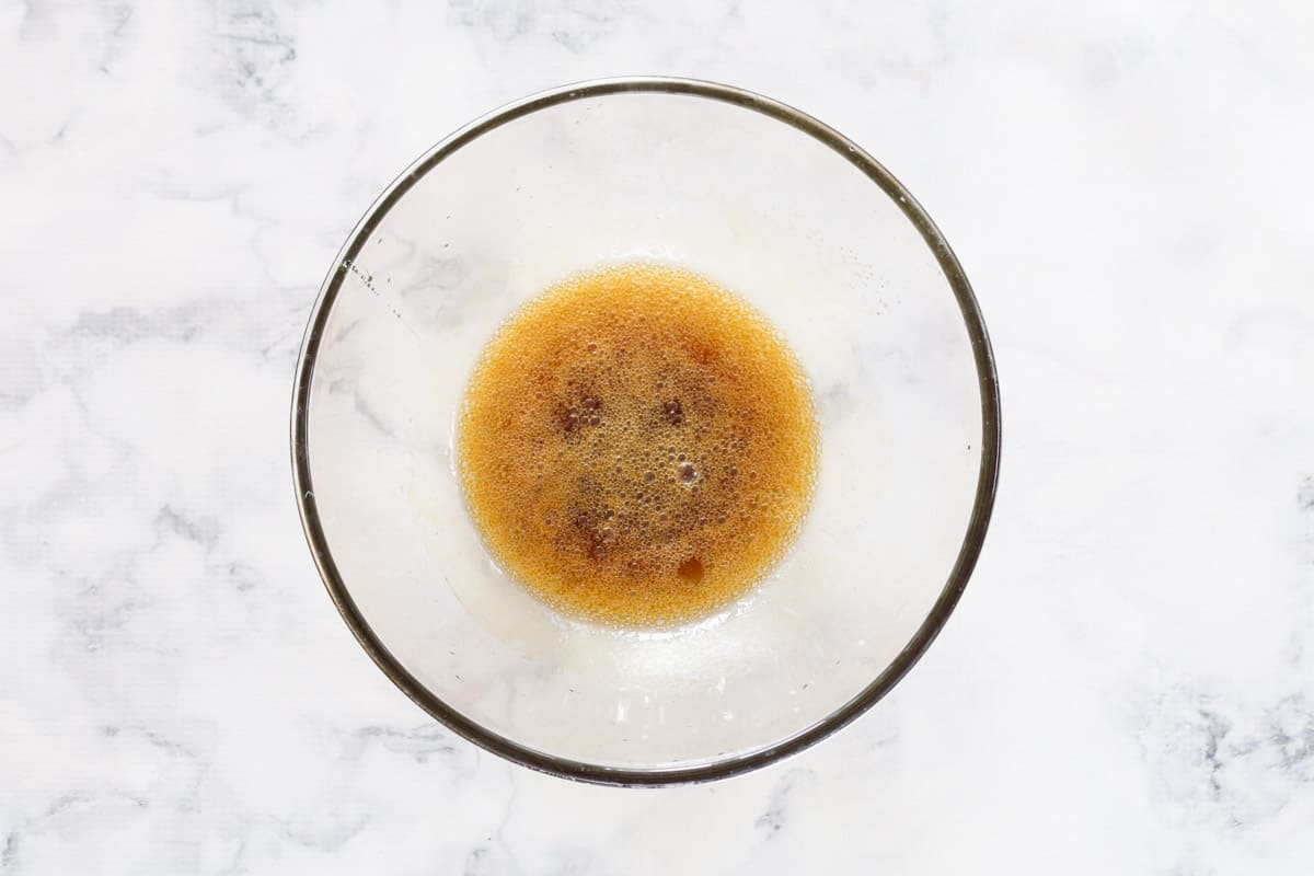 Coconut oil, brown sugar, honey, vanilla and salt melted together in a glass bowl on a marble counter