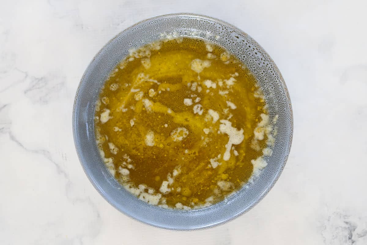 A speckled bowl with melted butter and honey on a marble countertop