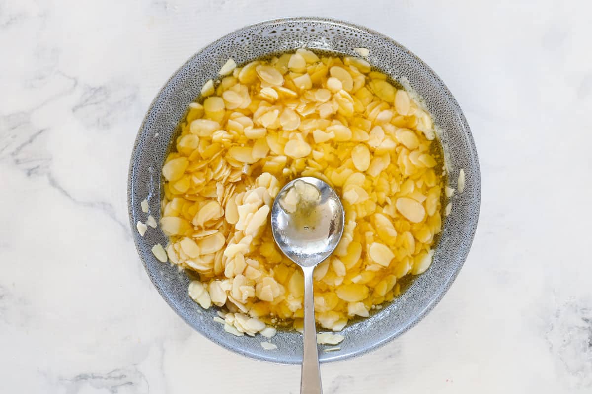 Flaked almonds being combined with melted butter in a bowl