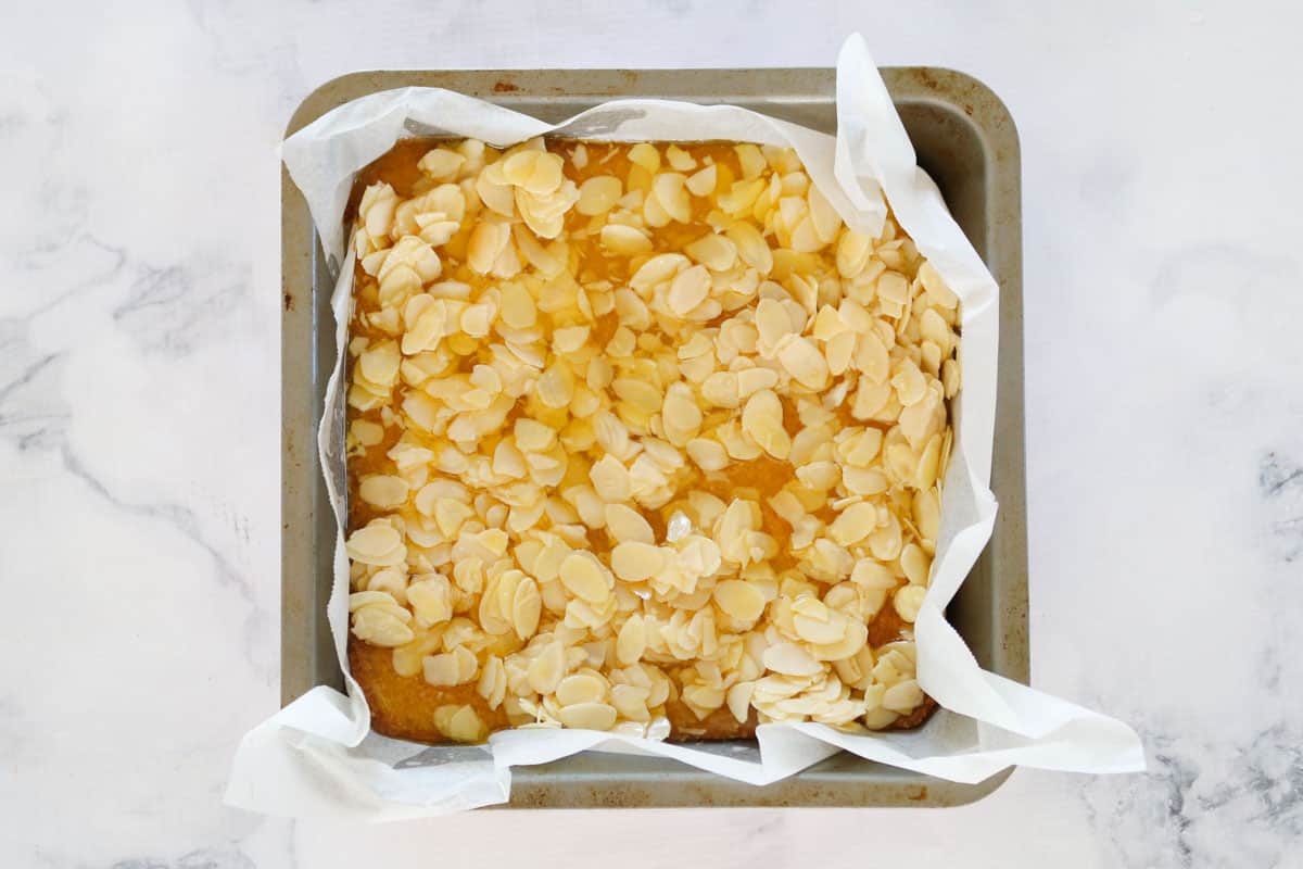 Flaked almond topping sprread over slice base in a lined square baking tin