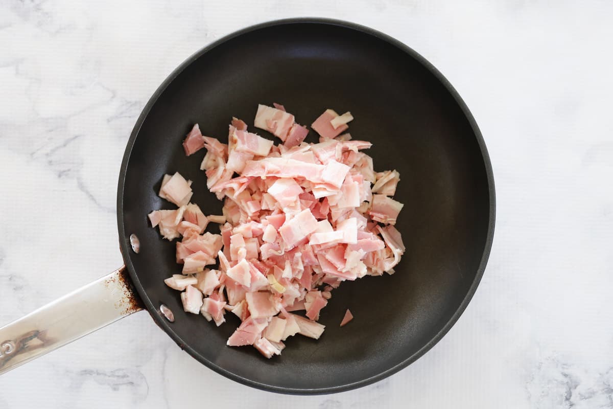A small frying pan with chopped bacon on a marble counter