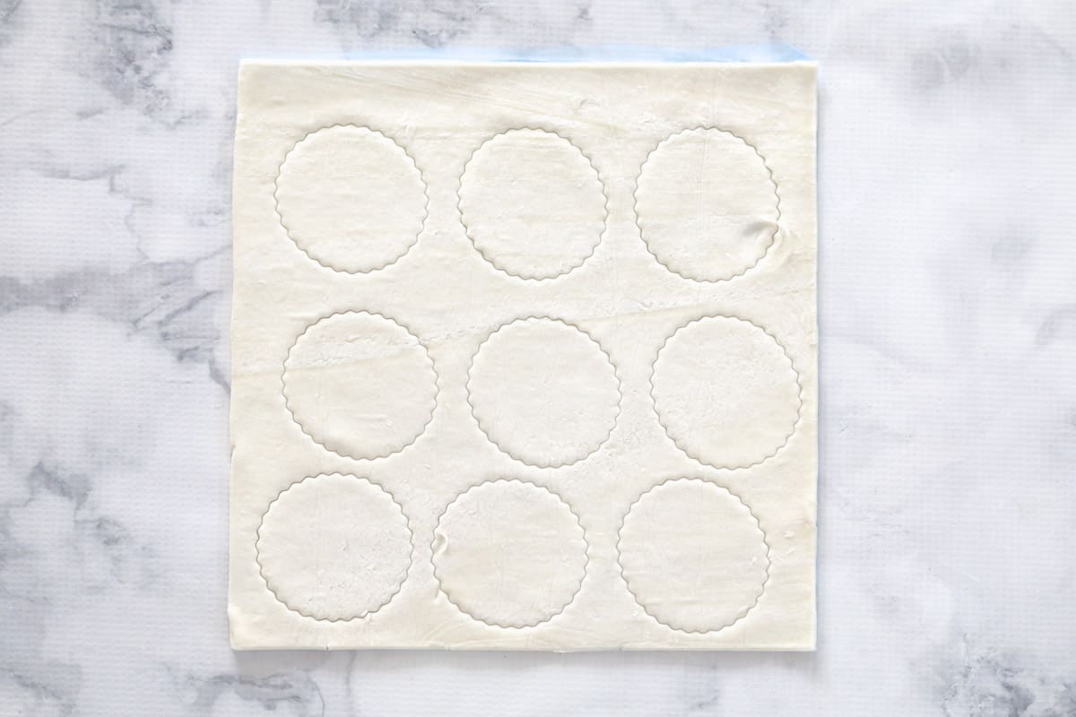 A sheet of puff pastry with circles cut out of it, on a marbled countertop