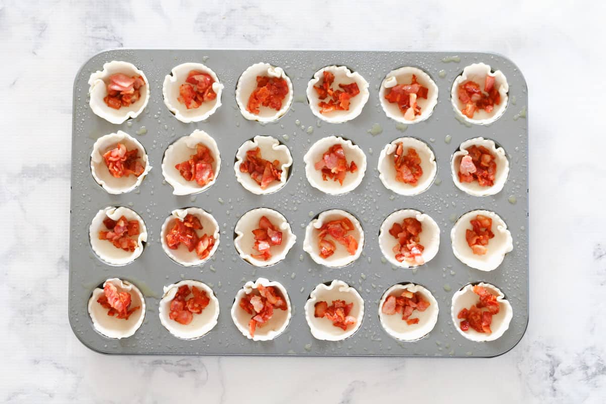 Puff pastry circles in a mini muffin tin filled with chopped fried bacon pieces