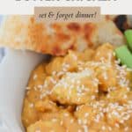 A bowl of creamy butter chicken, sprinkled with sesame seeds, and served with green beans and naan bread.