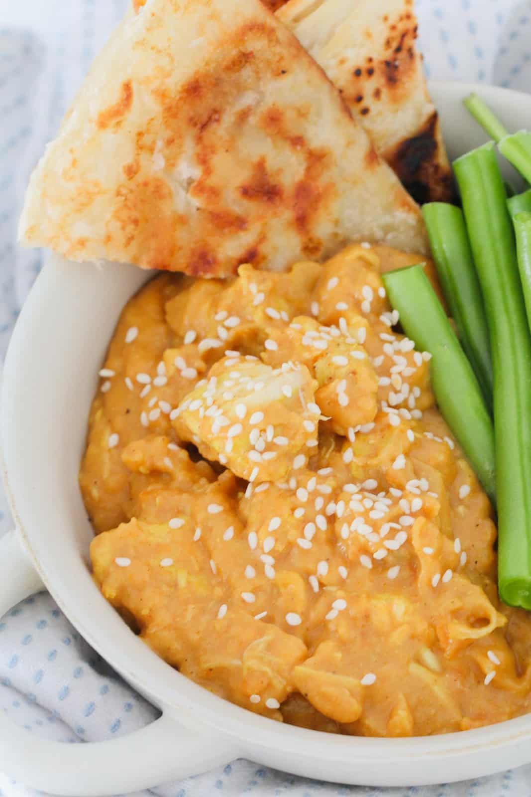 Creamy butter chicken in a bowl served with green vegetables and roti bread.