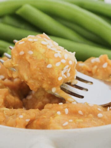 A piece of butter chicken on a fork with green vegetables.