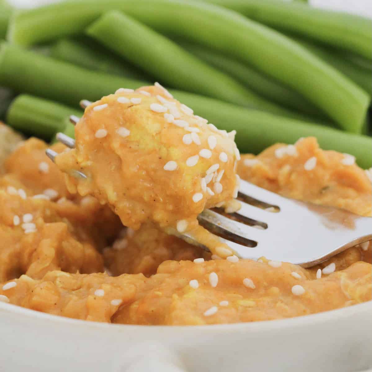 A piece of butter chicken on a fork with green vegetables.