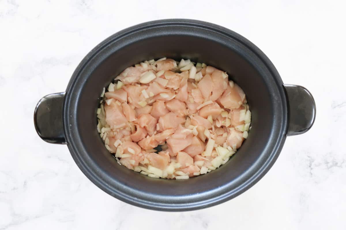 Diced onion and chicken in a slow cooker.
