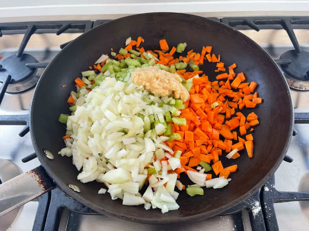 A non stick frying pan on a stove top with diced onion, carrot and celery and minced garlic.
