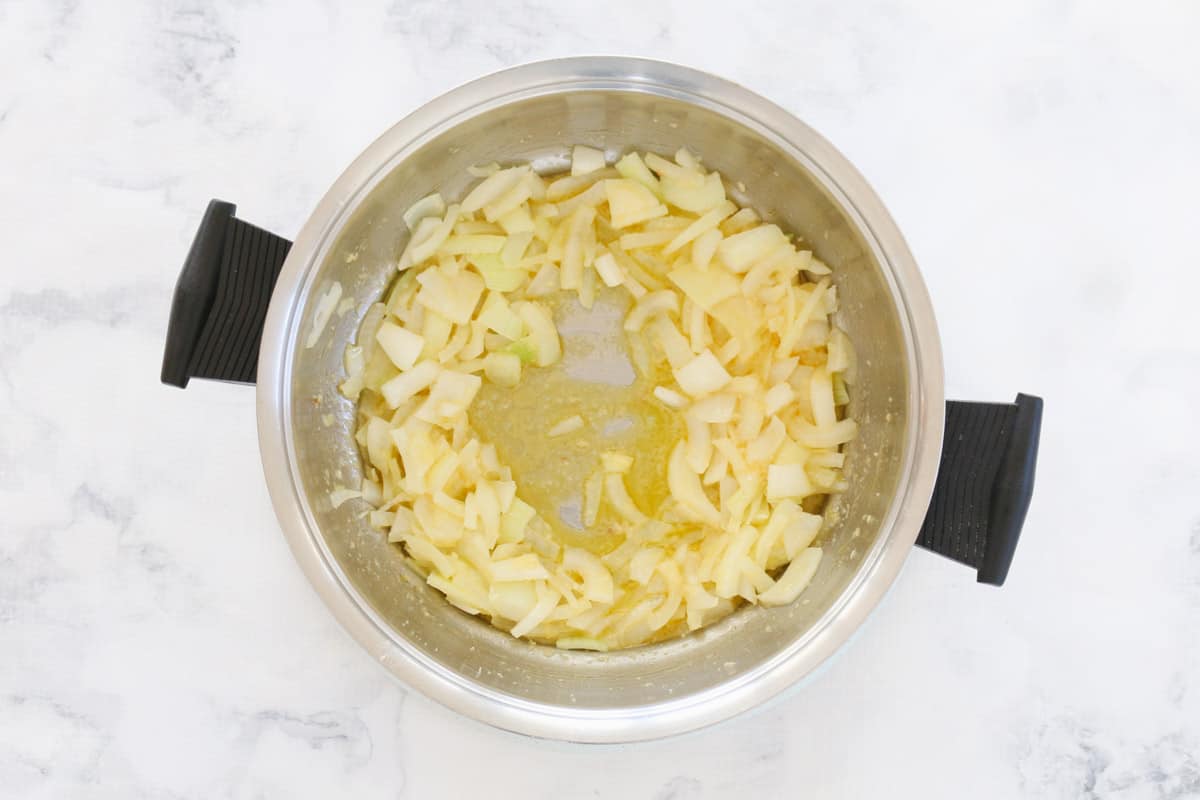 A black handled saucepan with chopped onions and minced garlic sautéing in butter.
