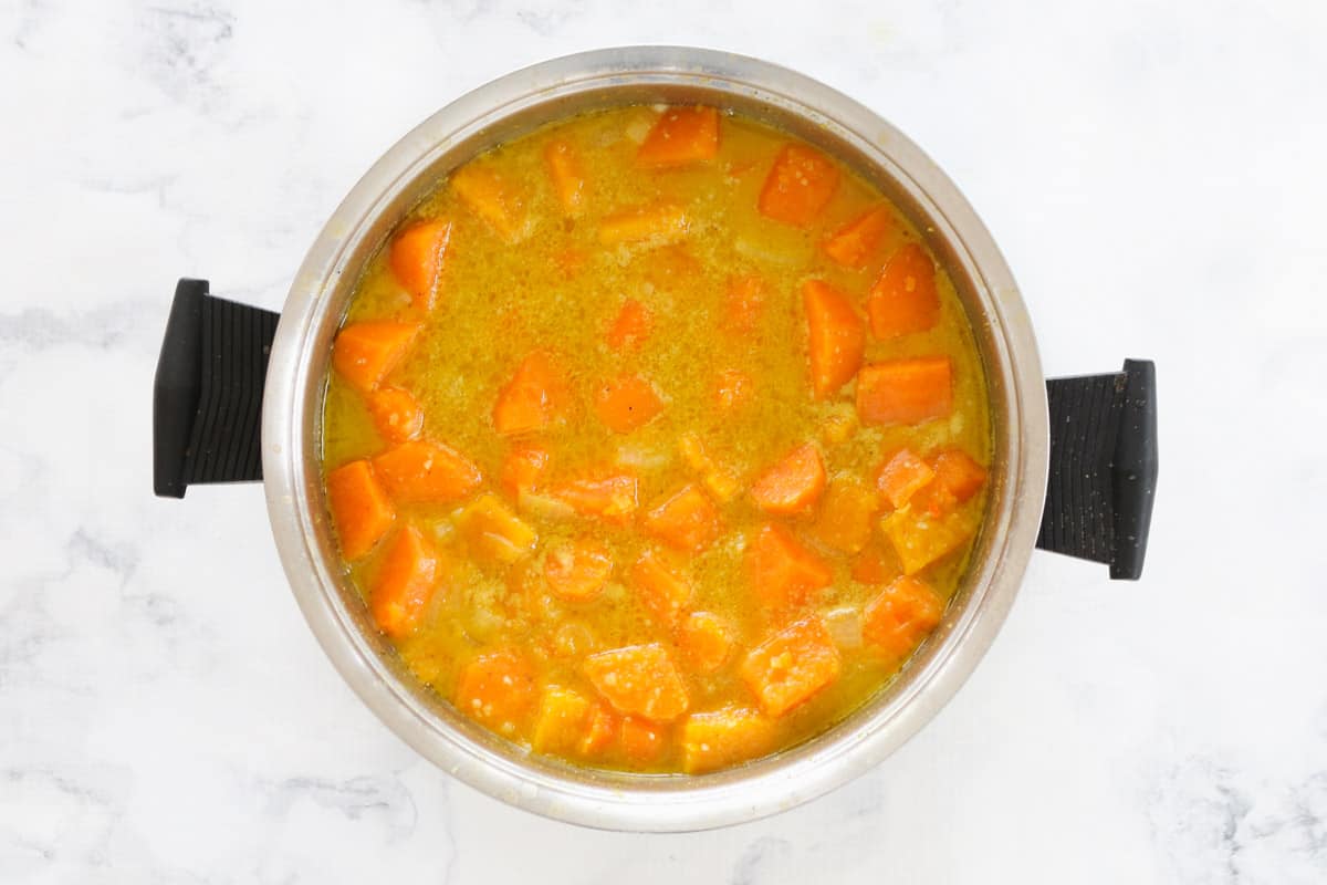 Chopped orange vegetables cooked down in liquid stock in a black handled saucepan