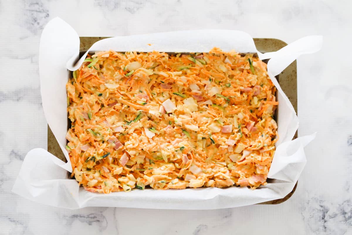 Uncooked zucchini and sweet potato slice in a baking paper lined rectangular baking tin