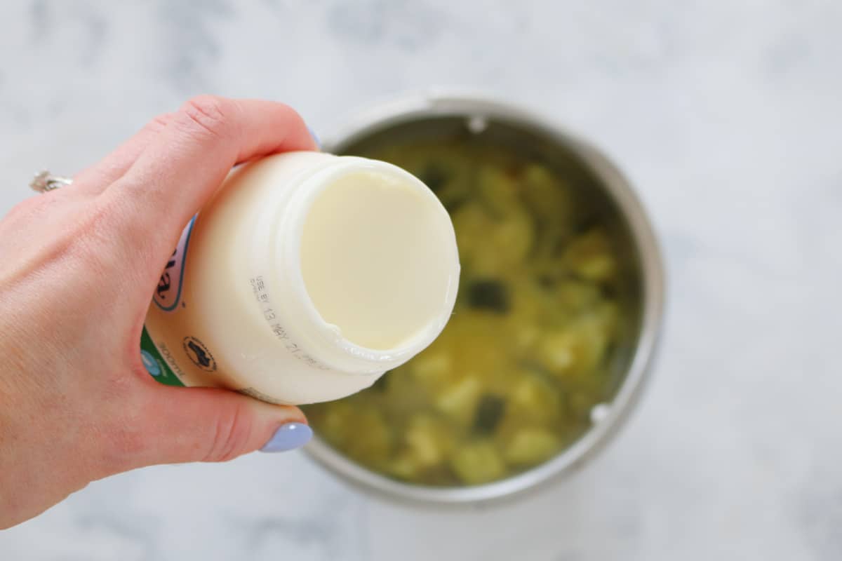 Cream being poured into blender filled with cooked zucchini and stock