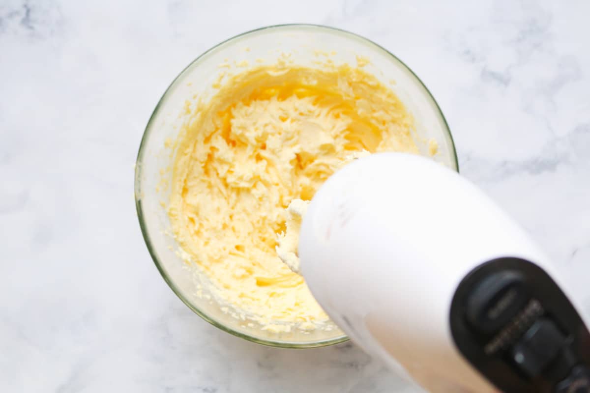 Beaters mixing together butter and sugar in a large bowl.