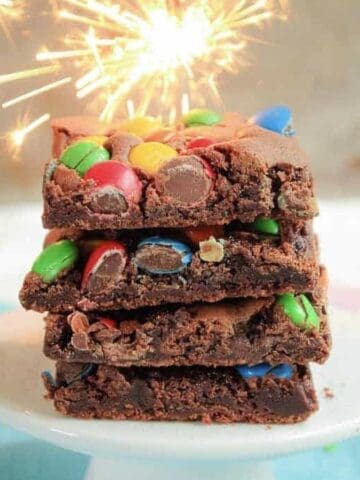 Front view of a stack of brownies with M&Ms and sparkler in background