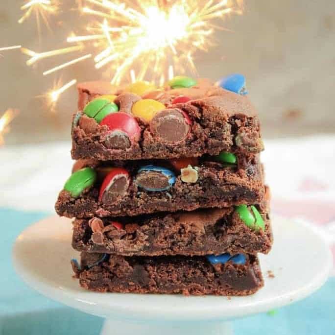 Front view of a stack of brownies with M&Ms and sparkler in background