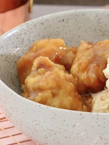 Sweet dumplings in a golden syrup sauce in a bowl with ice cream.