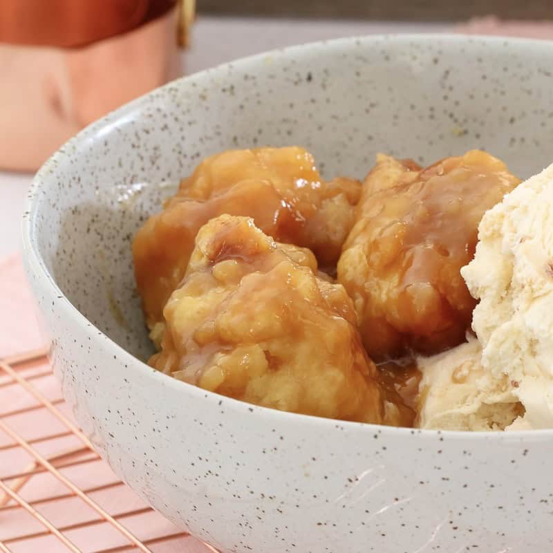 Sweet dumplings in a golden syrup sauce in a bowl with ice cream.