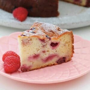 Front view of slice of cake on pink plate with two raspberries