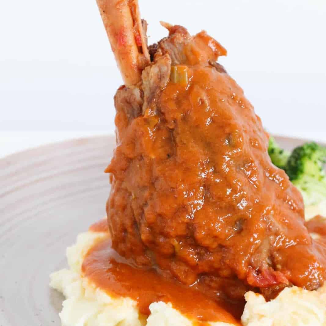 A close up image of a slow cooker lamb shank on mashed potato