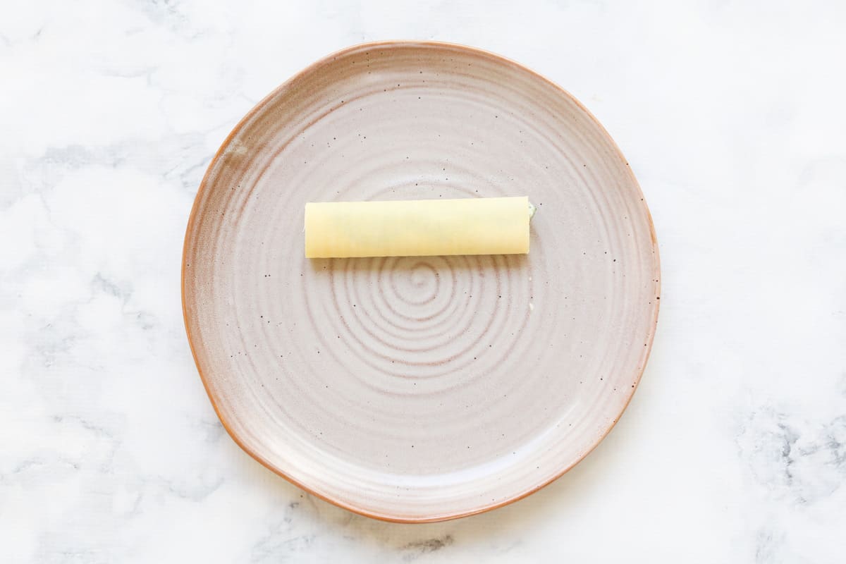 An earthenware plate on a marble counter with a rolled sheet of fresh pasta