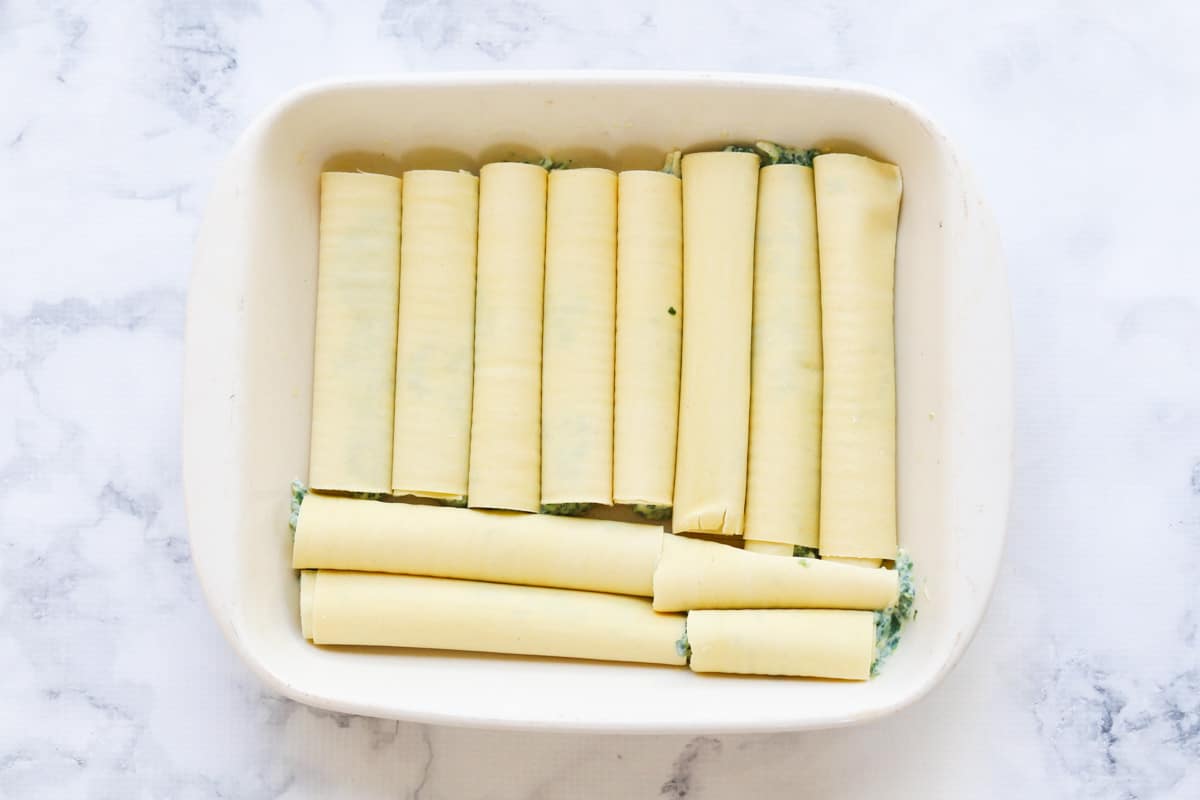 A white baking dish with rolled up tubes made of pasta sheets with a filling