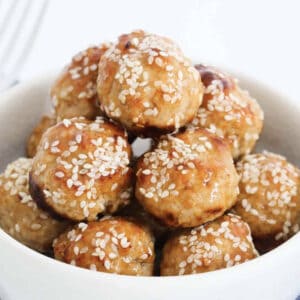 A bowl of chicken meatballs covered in sauce and sesame seeds.