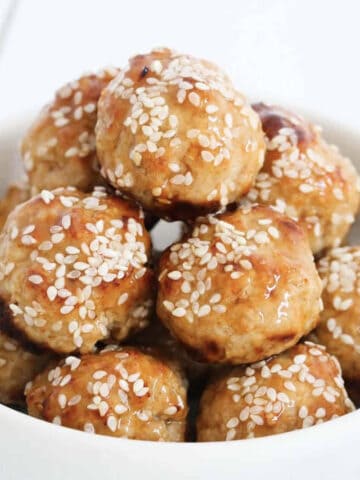 A bowl of chicken meatballs covered in sauce and sesame seeds.
