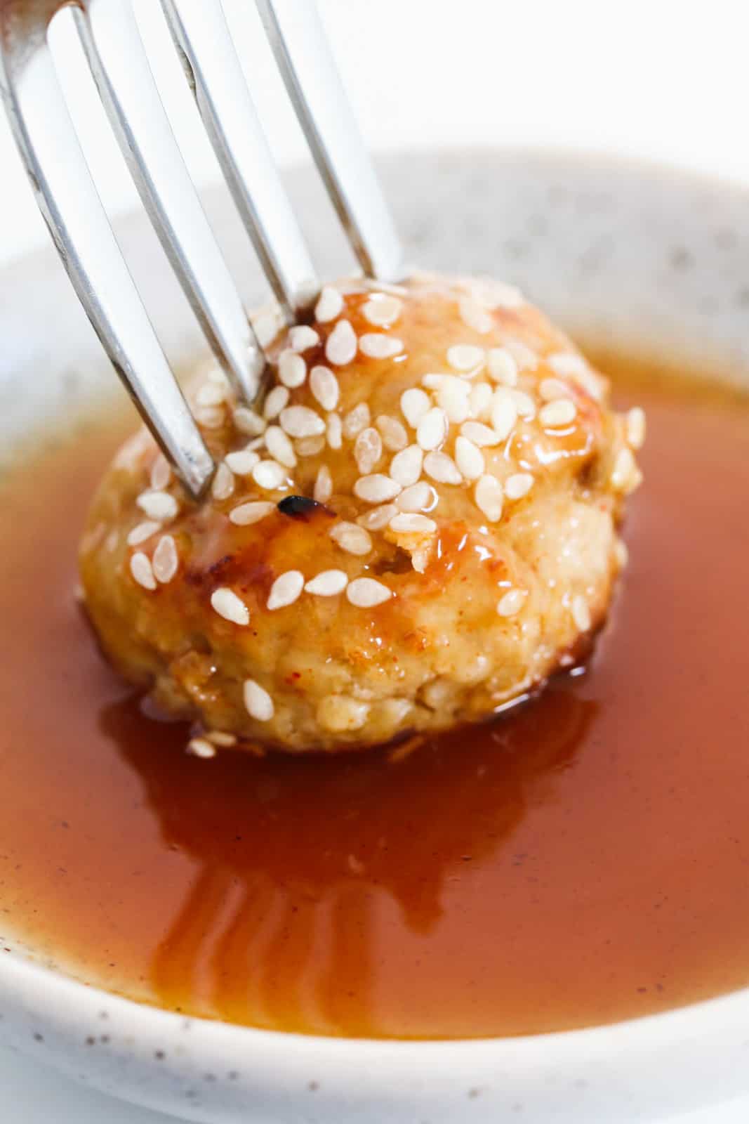 A chicken meatball being dipped into a sweet chilli and lime sauce.