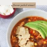A bowl of mexican chicken soup, with tortilla chips and sliced avocado on top.