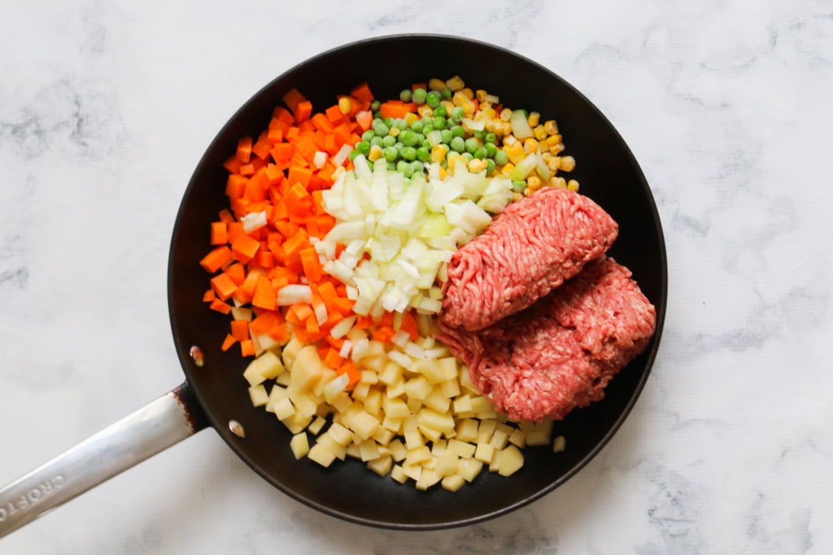 A frying pan with mince and finely diced vegetables on a marble countertop