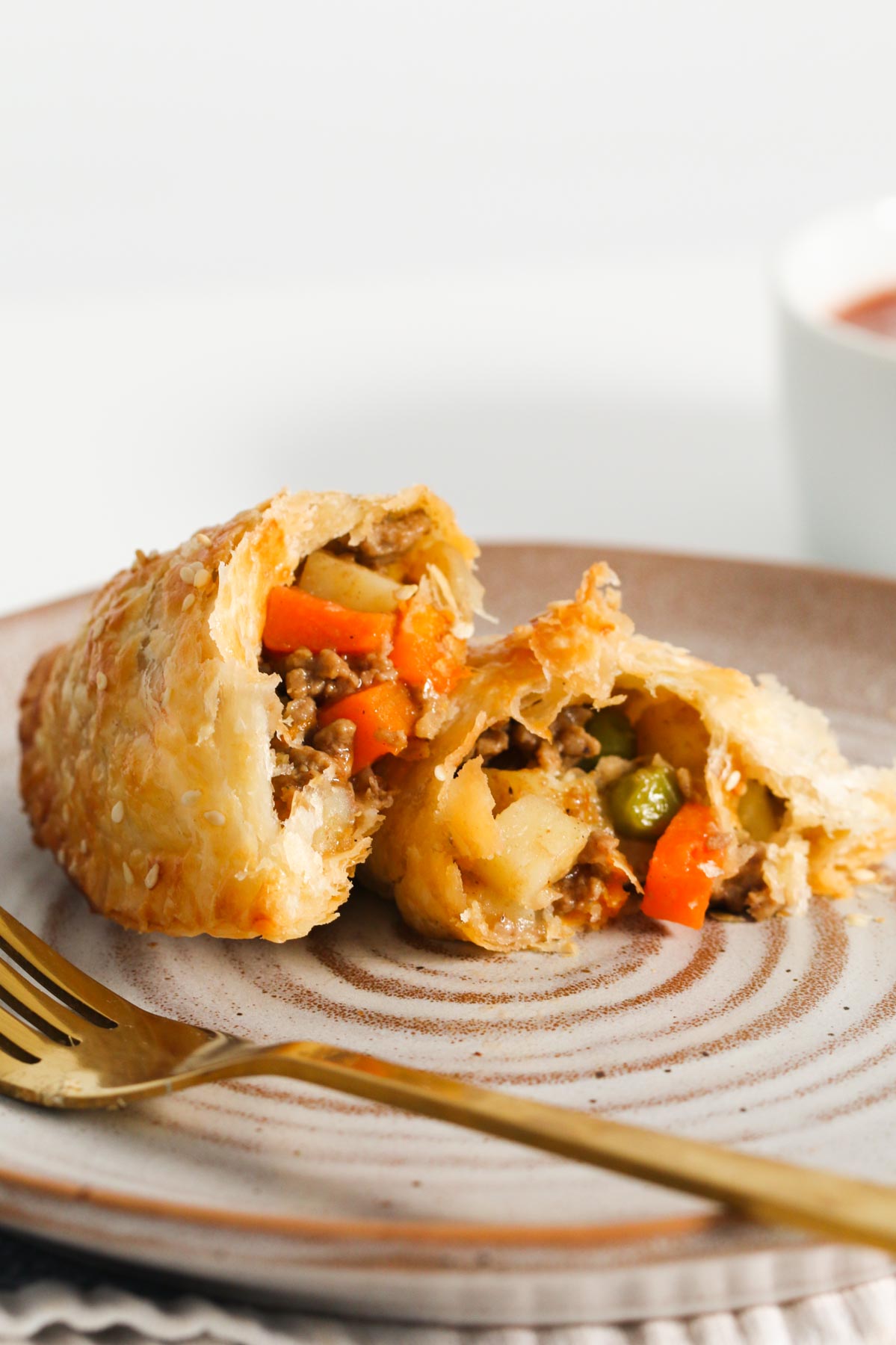 A savoury pastry, broken open to show the mince and vegetables inside, on a plate with a gold fork.