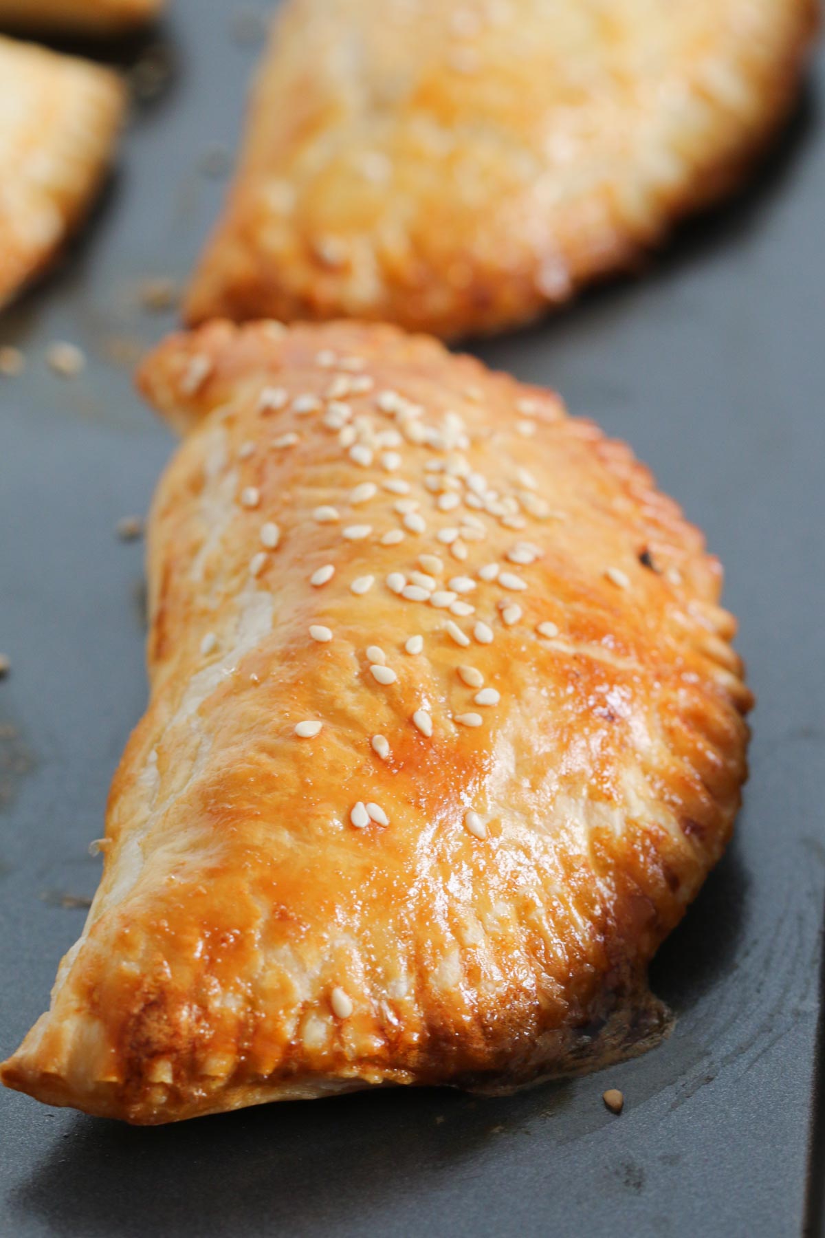 A close up of golden brown, sesame sprinkled, pasties on a baking tray