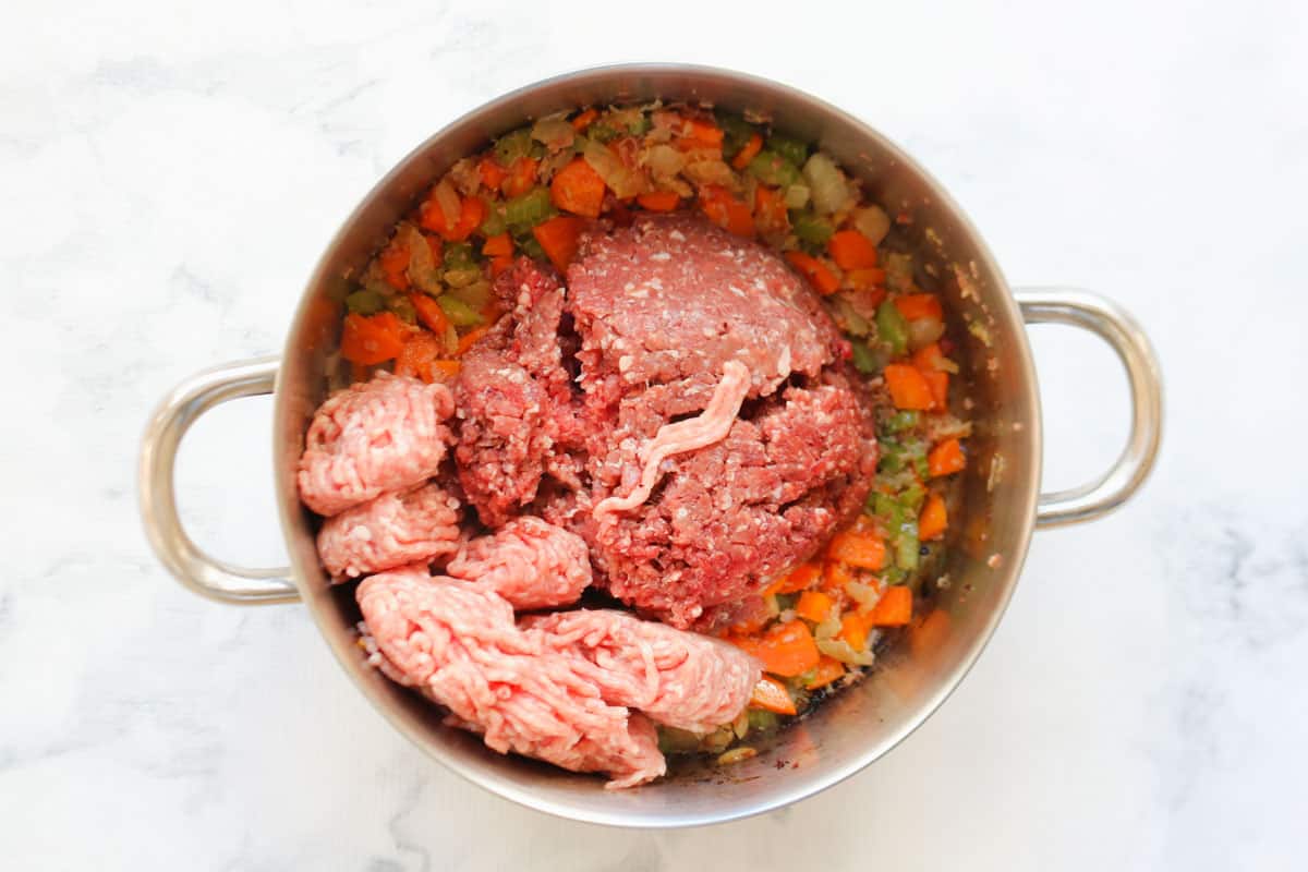 Pork and beef mince being added to sauteed vegetables.