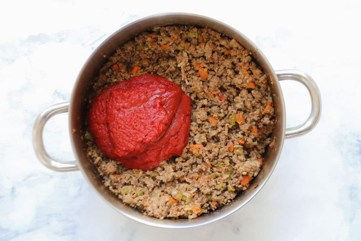 Tomato paste being added to a meat mixture in a pot.